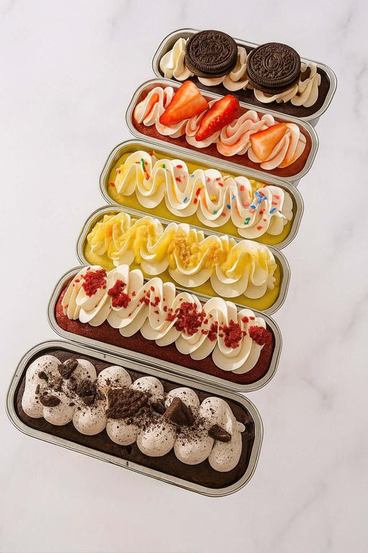 Artisan mini cakes with assorted toppings: cookies, strawberries, sprinkles, and gold-dusted glaze on a white marble background.